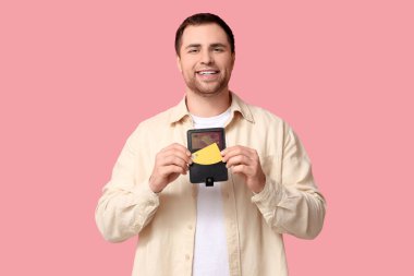 Pembe arka planda kredi kartı olan genç bir adam cüzdanı tutuyor.