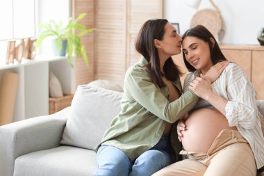 Evdeki kanepede hamile karısını öpen genç lezbiyen kadın.