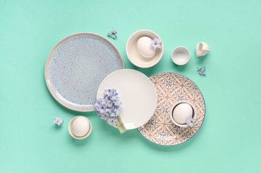 Paskalya yumurtaları, çiçekler ve turkuaz arka planda oyuncak tavşanlarla süslü masa.