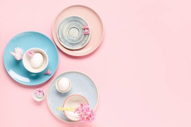 Paskalya yumurtaları, çiçekler ve pembe arka planda oyuncak tavşanlı şık bir masa.