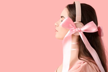 Pembe arka planda fiyonklu, kulaklıklı güzel bir genç kadın.