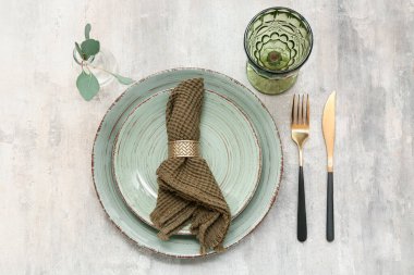 Altın çatal bıçak takımları ve gri arka planda yaprakları olan güzel bir masa.