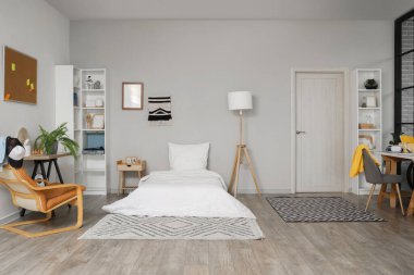 Öğrenci odasının içinde yatak, koltuk ve raf üniteleri var.