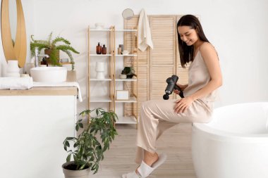 Banyoda bacağına perküsyon masajıyla masaj yapan genç bir kadın.