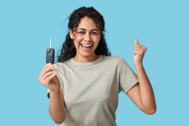 Mavi arka planda araba anahtarı olan mutlu bir Afro-Amerikalı kadın.