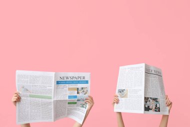 Pembe arka planda gazeteleri olan kadın eller.