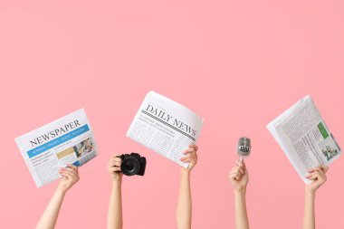 Gazeteli, mikrofonlu ve pembe arka planda fotoğraf makinesi olan kadın eller.