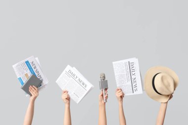 Gazeteleri, mikrofonu ve gri arka planda şapkası olan kadın elleri.