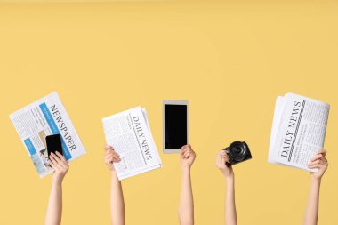 Gazeteli kadın eller ve sarı arka planda modern cihazlar.