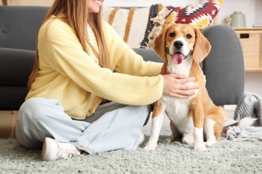 Genç bir kadın oturma odasında yerde köpeğini okşuyor.