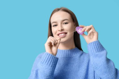 Mavi arka planda diş ipi olan genç bir kadın, yakın plan.