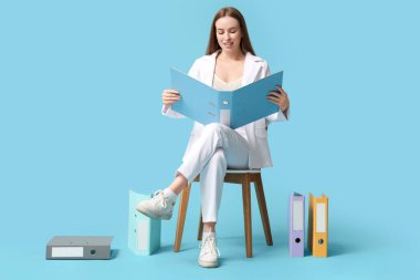 Mavi arka planda duran belge klasörlü genç iş kadını