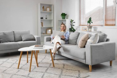 Genç bir kadın oturma odasındaki koltukta dizüstü bilgisayar kullanıyor.