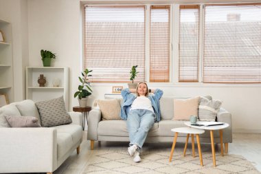 Genç bayan oturma odasındaki kanepede dinleniyor.