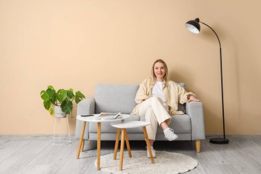 Bej oturma odasında, kanepede oturan genç bir kadın.