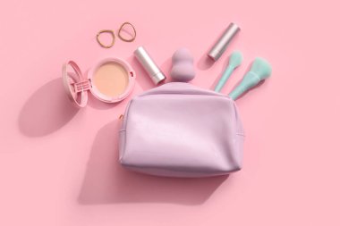 Makyaj ürünleri ve pembe arka planda aksesuarları olan kozmetik çanta.