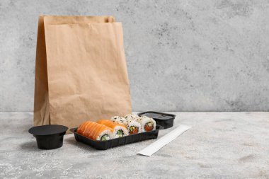 Hafif grunge arka planında lezzetli suşi ruloları, yemek çubukları ve kağıt torba olan plastik tabak. Teslimat konsepti
