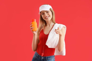 Young female lifeguard in cap with towel and sunscreen on red background clipart