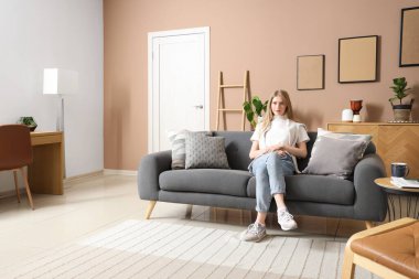 Şık bir oturma odasında kanepede oturan genç bir kadın.