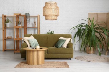 Beyaz oturma odasının içinde yeşil kanepe, yastıklar, lamba ve sehpa var.