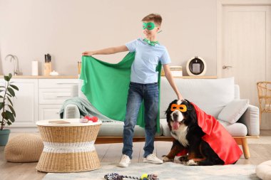 Tatlı tüylü köpek ve süper kahraman kostümlü çocuk oturma odasındaki kanepenin yanında.