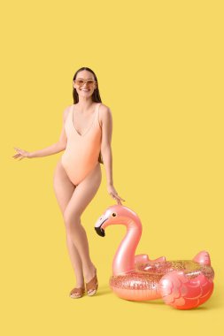 Güneş gözlüklü gülümseyen kadın ve sarı arka planda şişirilebilir yüzük.