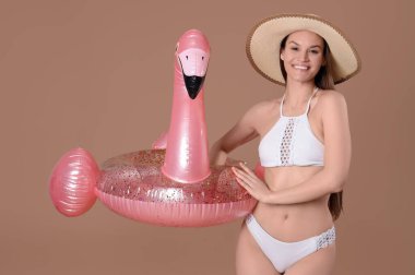 Kahverengi arka planda şişirilebilir yüzüğü olan mayo giymiş gülümseyen genç bir kadın.