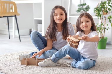 Küçük şirin Asyalı mutlu kız kardeşler tahta uçaklarla yerde oturuyor ve evde oynuyorlar.