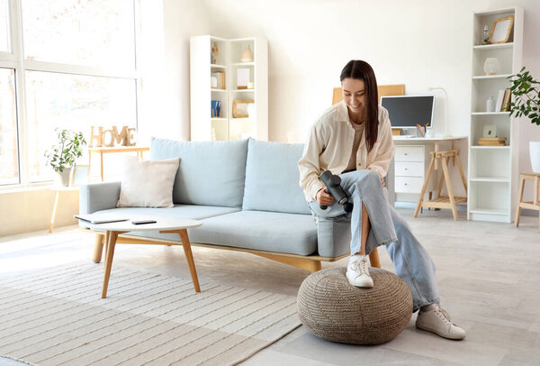 Young woman massaging her leg with percussive massager at home