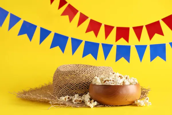 stock image Bowl of tasty popcorn, straw hat and flags for Festa Junina celebration on yellow background