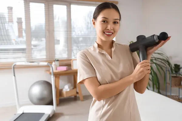 stock image Female Asian physiotherapist with percussive massager in rehabilitation center