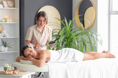 Masaj terapisti spa salonunda genç bir kadının sırtına çamur sürüyor.