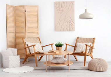 Beyaz oturma odasının içinde rahat koltuklar, sehpa ve resim.