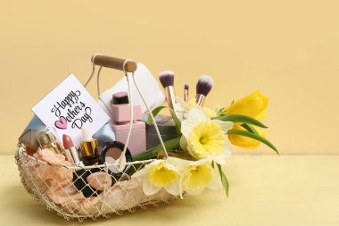 Süslü makyaj malzemeleri, makyaj fırçaları ve narsist çiçeklerle dolu hediye sepeti. Anneler günü için renkli ahşap masada.