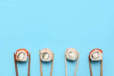 Lezzetli suşili çubuklar mavi arka planda yuvarlanıyor.
