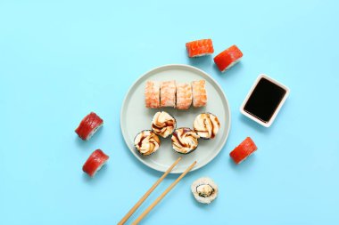 Lezzetli suşi ruloları, yemek çubukları ve mavi arka planda soya soslu bir tabak.