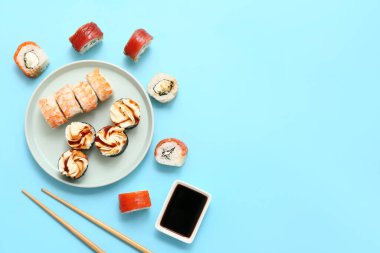 Lezzetli suşi ruloları, yemek çubukları ve mavi arka planda soya soslu bir tabak.