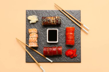 Lezzetli suşi ruloları, salamura zencefil, yemek çubukları ve bej arka planda soya sosu.