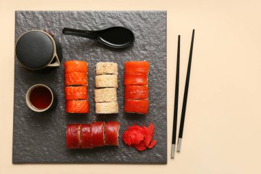 Lezzetli suşi ruloları, yemek çubukları, çaydanlık ve bej arka planda bir fincan çay.