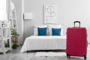 Yatağın yanında bavulu olan hafif bir otel odası.