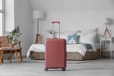 Suitcase near bed in light hotel room