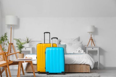 Yatağın yanında bavulları olan hafif bir otel odası.