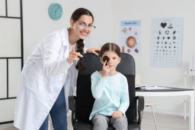 Female ophthalmologist and little girl with occluder checking eyesight in clinic clipart