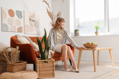 Beyaz oturma odasındaki kahverengi kanepede oturan genç ve güzel bir kadın.