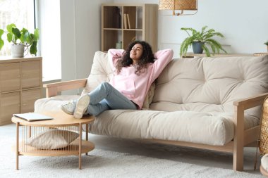 Genç Afro-Amerikalı kadın evdeki kanepede dinleniyor.