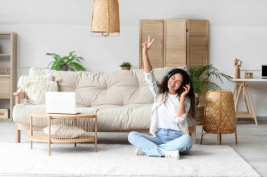 Kulaklıklı genç Afro-Amerikalı kadın evde yerde dinleniyor.