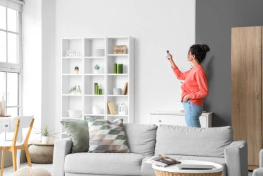 Genç Afro-Amerikalı kadın oturma odasında klimayı açıyor.