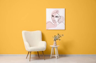 Turuncu duvarın yanındaki masada çiçek açan dalları olan koltuk ve vazo.