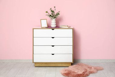 Boş fotoğraf çerçevesi ve vazo, pembe duvarın yanındaki çekmecelerin üzerinde çiçek açan güzel dallarla dolu.