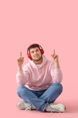 Kulaklıklı genç sakallı adam pembe arka plandaki bir şeyi işaret ediyor.